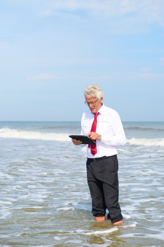 Man in business attire standing in ocean working on an ipad